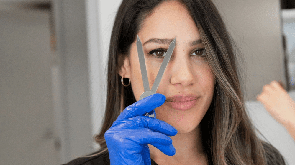 Hand of a woman with a blue surgical glove holding a metal accessory in front of her face